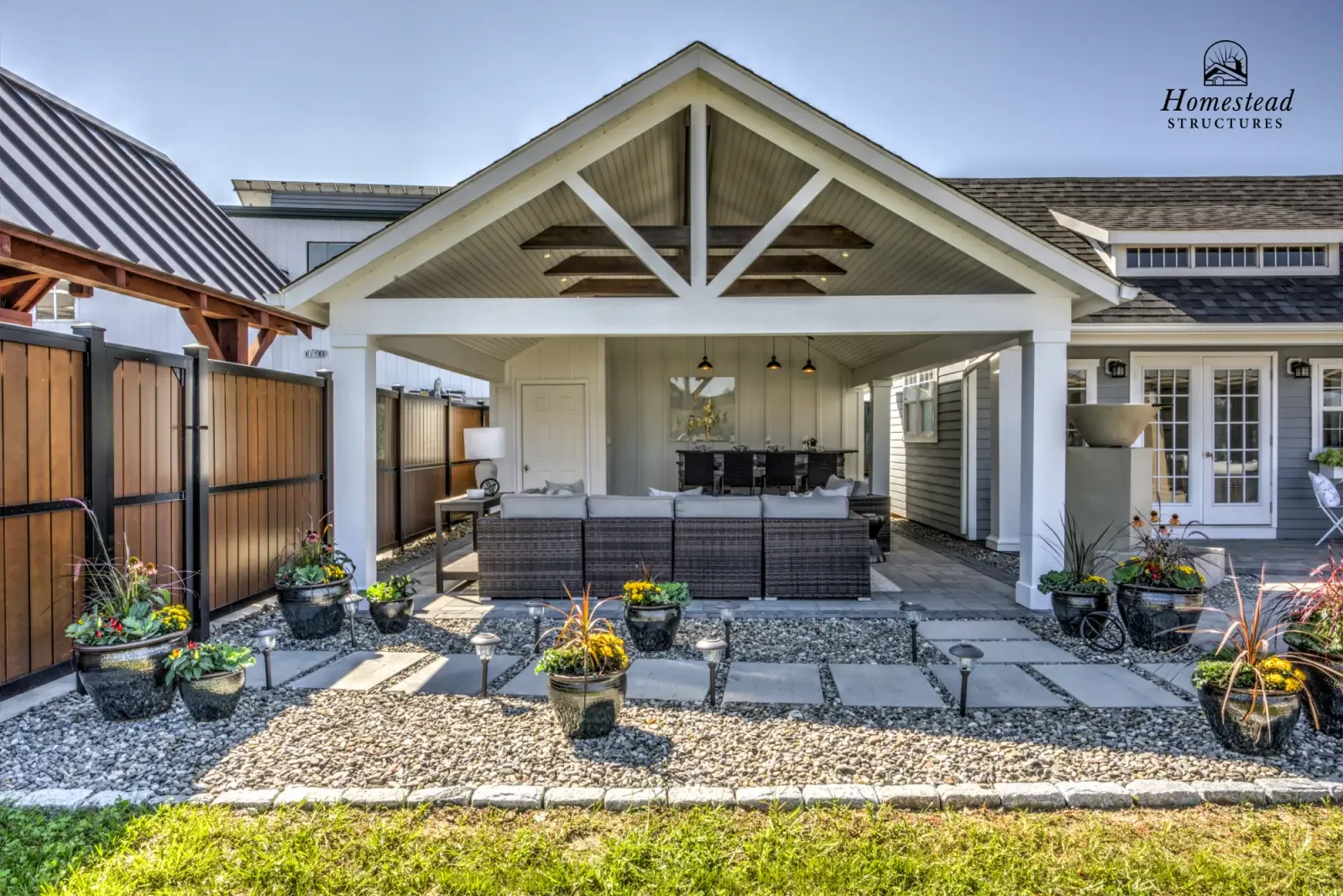 Covered outdoor patio with wicker furniture, potted plants, pathway, and surrounding house