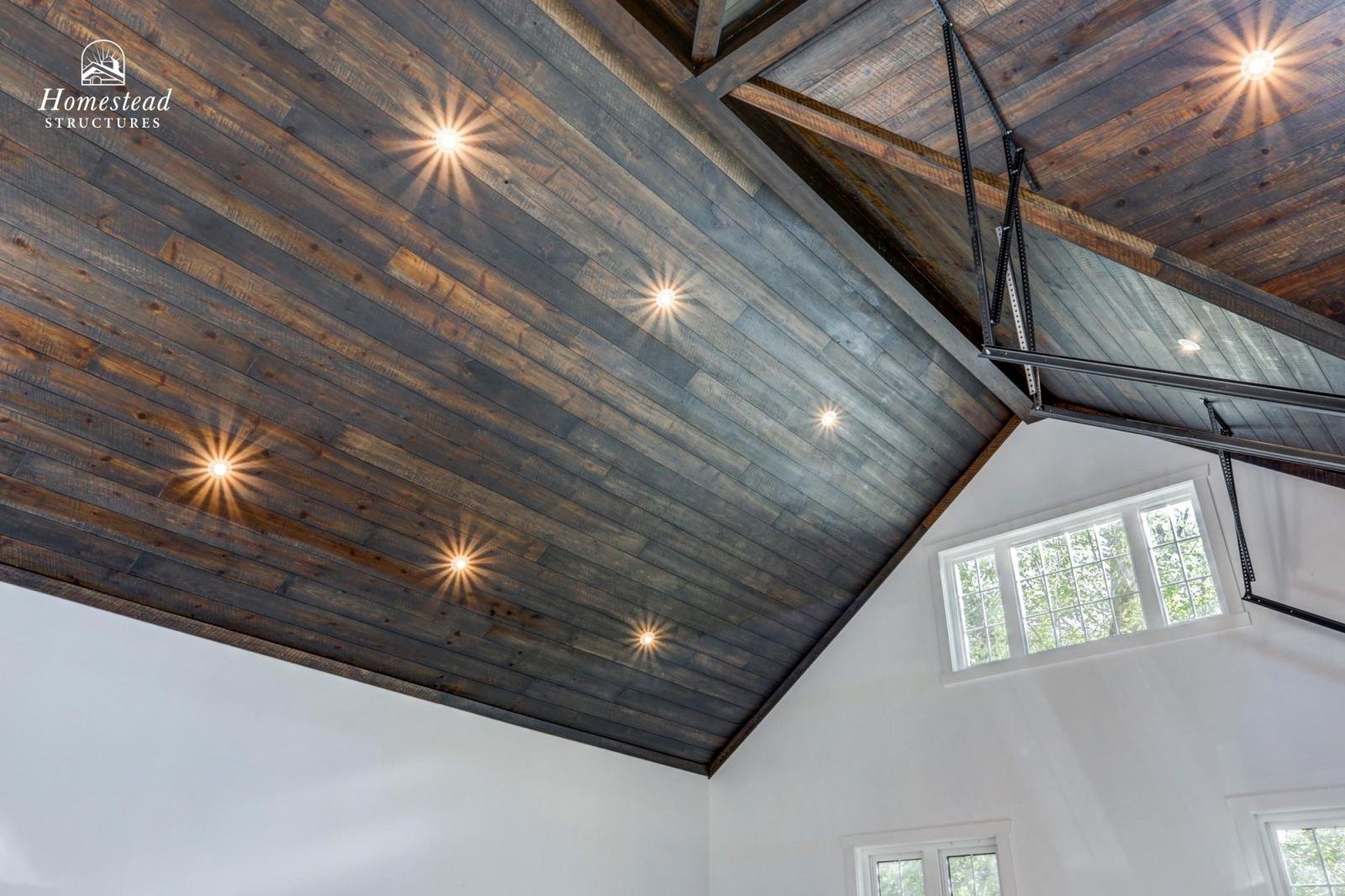 Interior view of a room with a wooden vaulted ceiling and recessed lighting, with a large window on the white wall below.