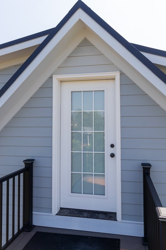 Exterior view of a house with a gray facade, white trim, and a white door with glass panels, black handrails on either side of a small porch.