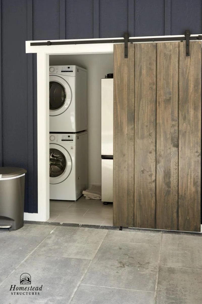Laundry closet with stacked washer and dryer behind a sliding wooden barn door.