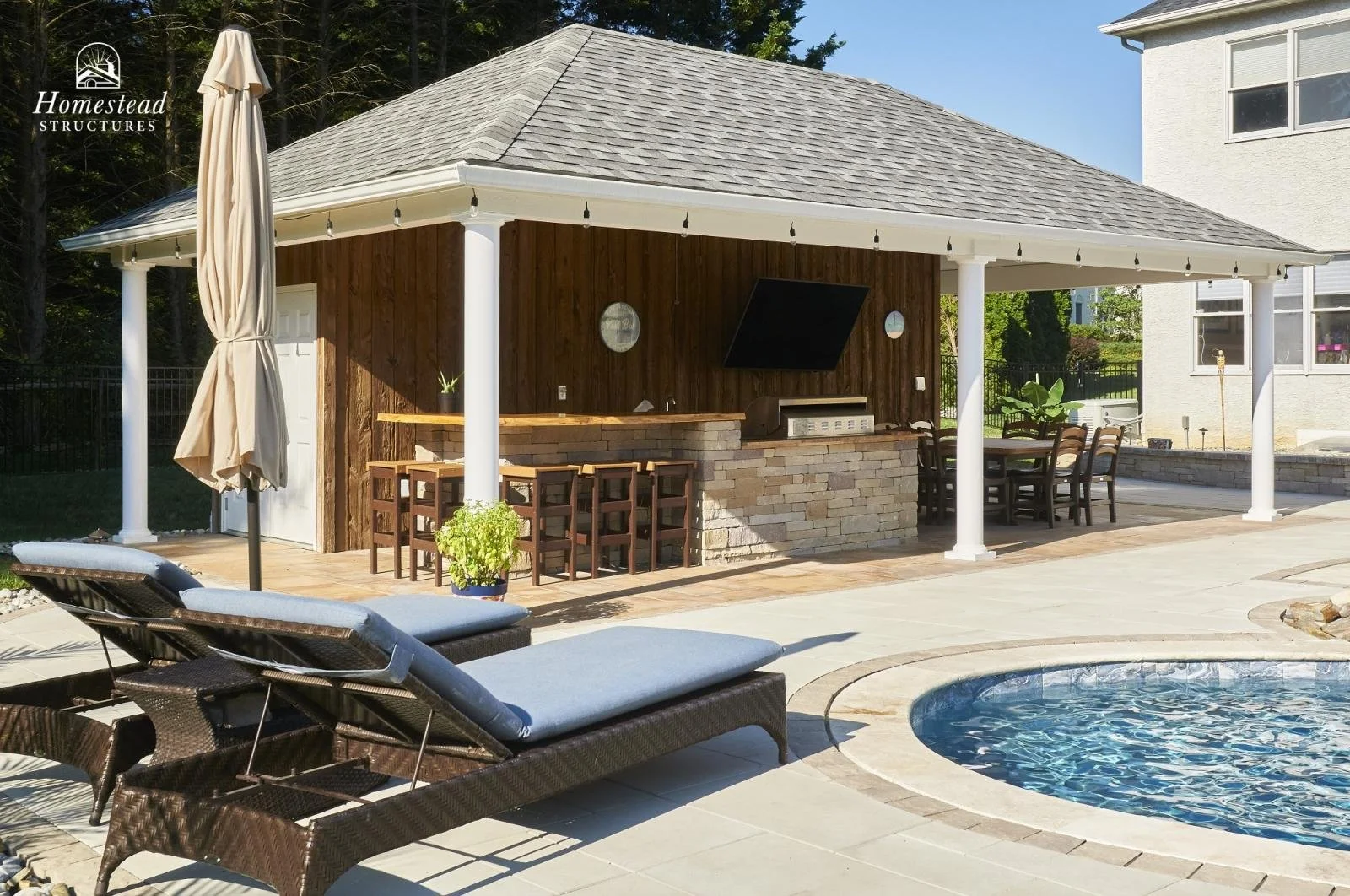 Backyard with pool, outdoor lounging chairs, a gazebo with a bar area, a dining table, and plants, under clear blue sky.