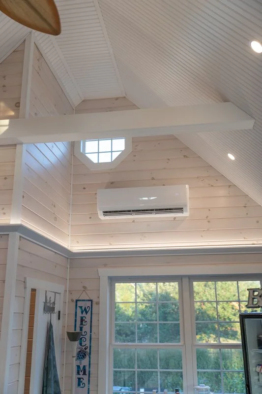 Interior of a room with high, vaulted ceilings, wooden walls, a window, air conditioner, and architectural lighting.