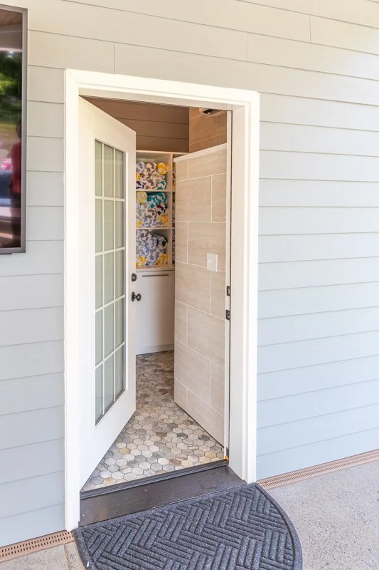 Open door leading to a storage closet with shelves of folded towels or linens, and a hexagonal tile floor.