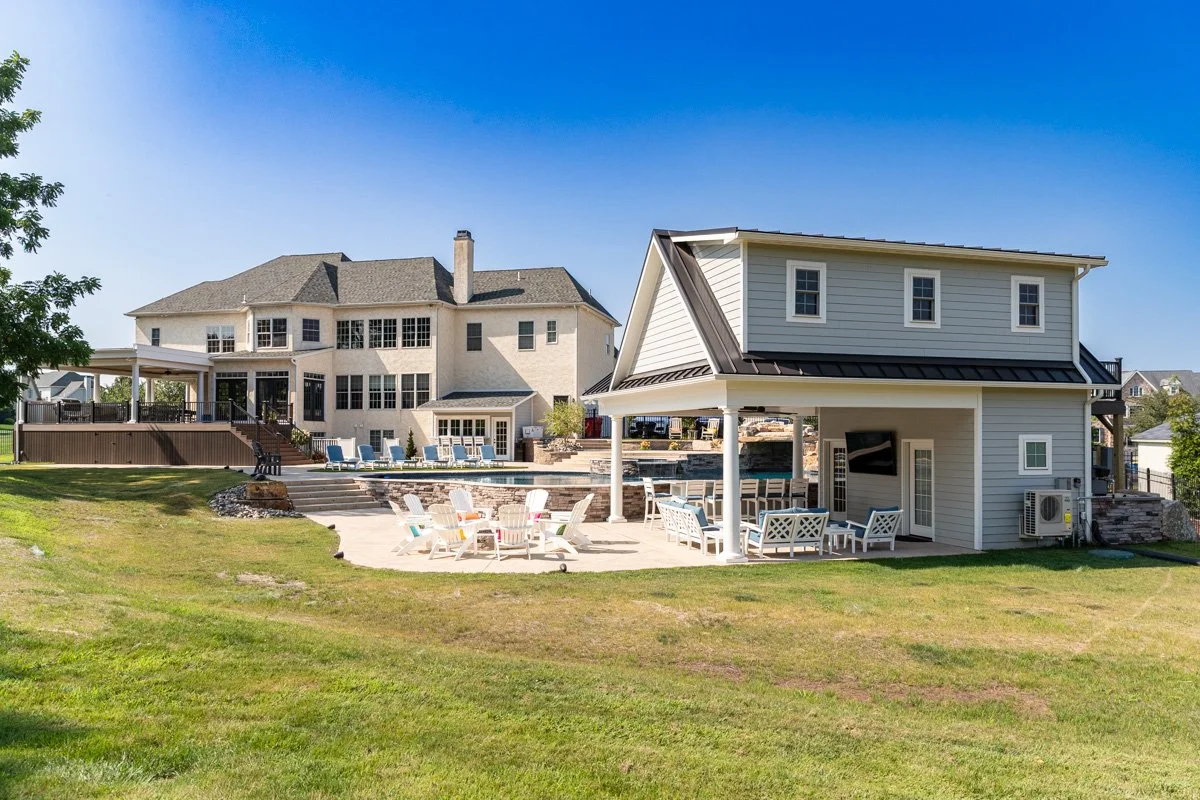 Backyard with large house, swimming pool, and covered outdoor seating area with chairs and a TV