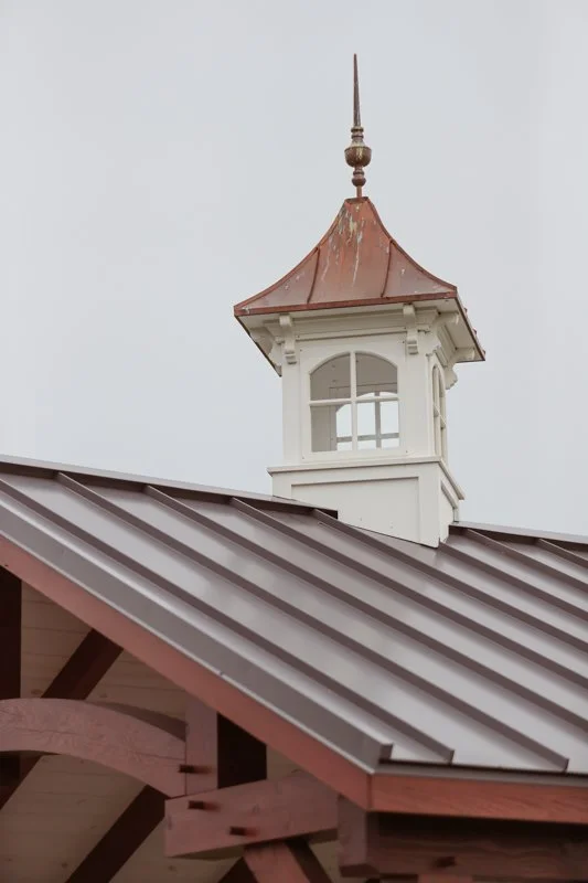 Close-up of a building's roof with a small tower with a pointed, copper-colored roof and a weather vane on top.