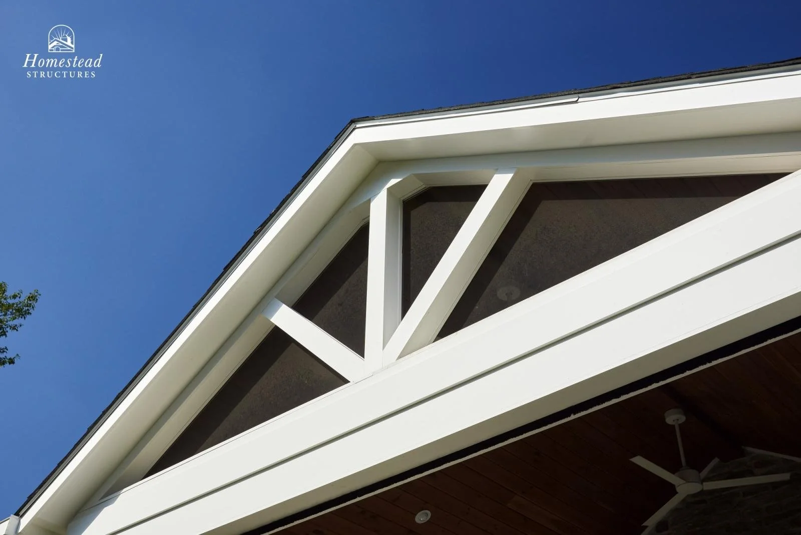 Close-up of the upper corner of a modern house with white framing, a gable roof, and a window, against a clear blue sky.