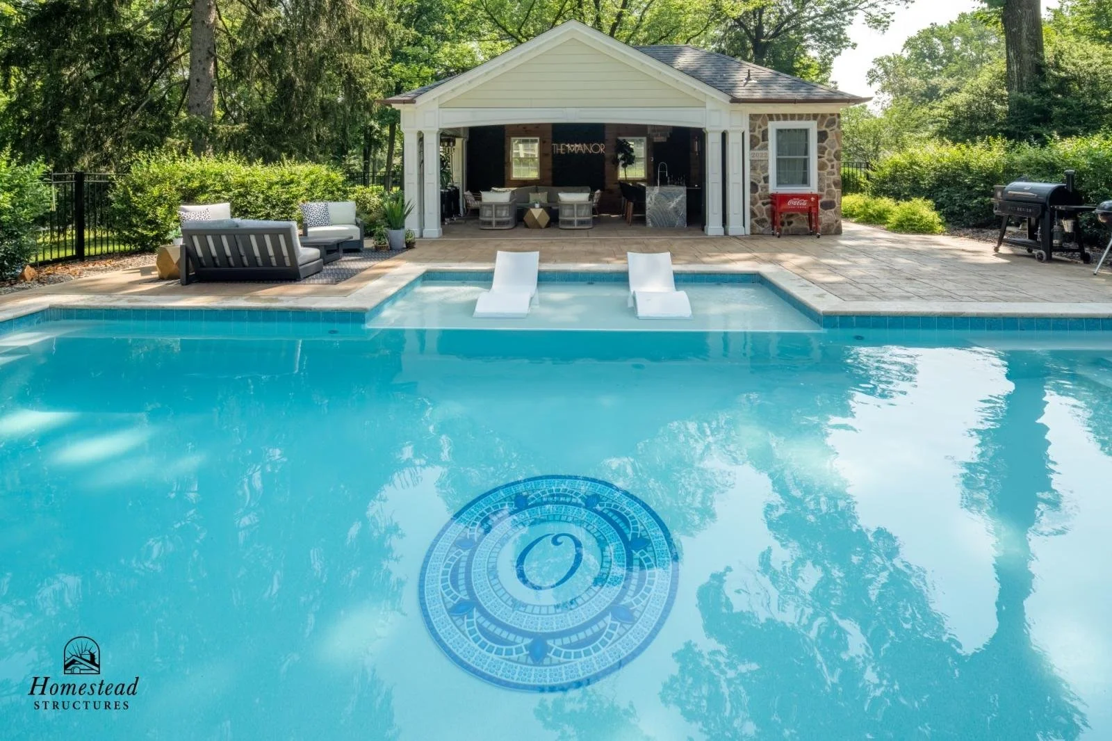 Backyard pool area with water slide and a pool house in the background, surrounded by greenery.