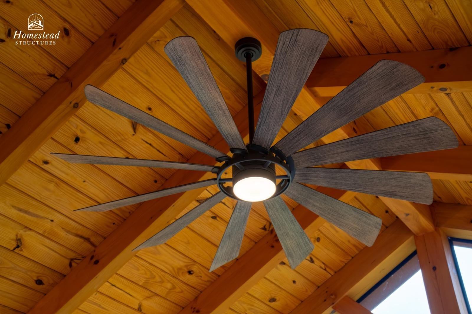 Ceiling fan with wooden blades and a built-in light fixture mounted on a wooden ceiling in a home interior.