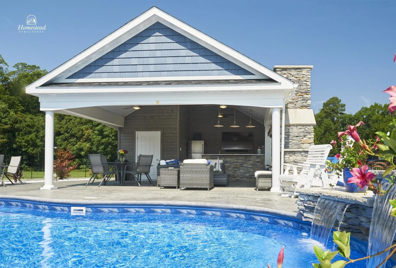 A backyard with a pool, an outdoor lounge area with chairs and a TV, a covered patio with a barbecue, and a small waterfall feature on the right, surrounded by greenery and flowers.