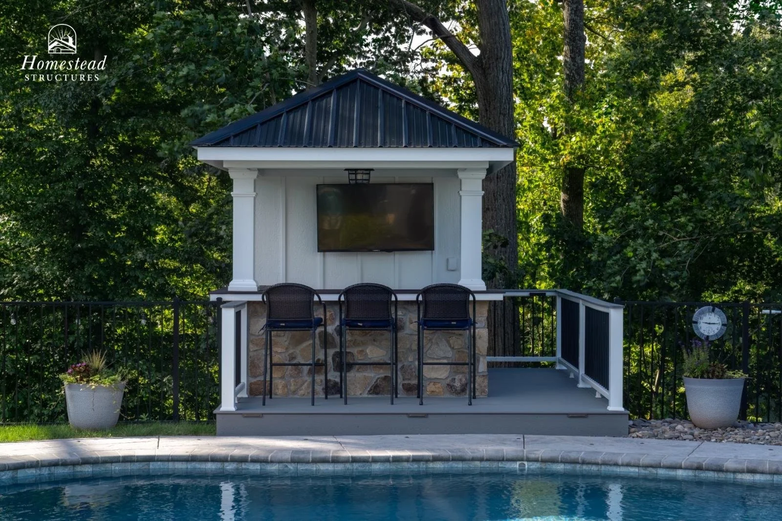 Outdoor pool area with a poolside bar and television, surrounded by greenery and potted plants.