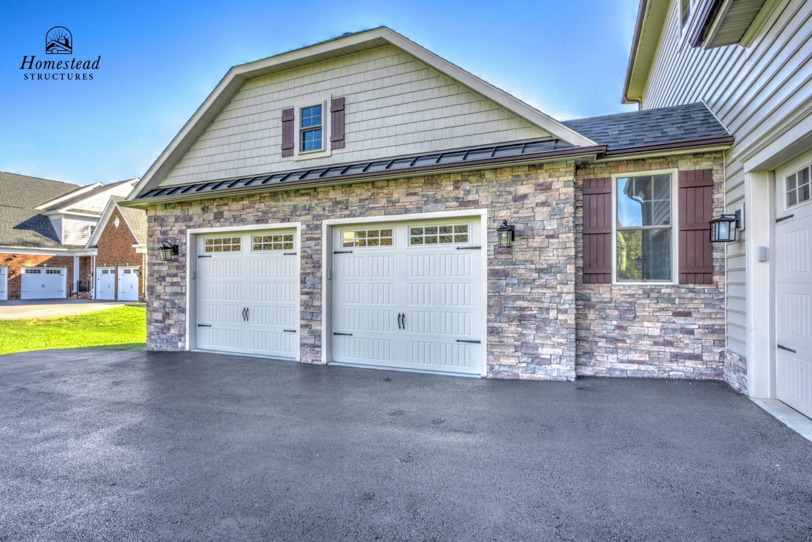 Exterior view of a house with a double garage, brick and stone facade, and a small window with brown shutters, under a clear blue sky.