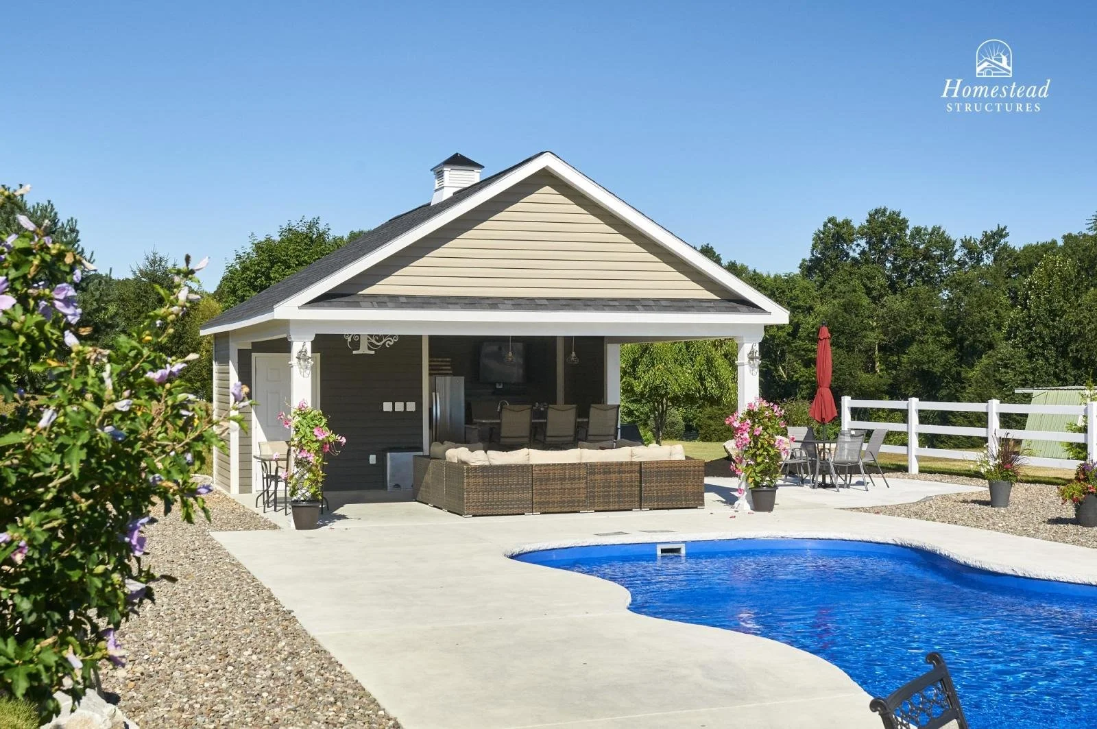 Backyard with swimming pool, outdoor seating area, and a house with a covered patio, surrounded by trees and greenery on a sunny day.
