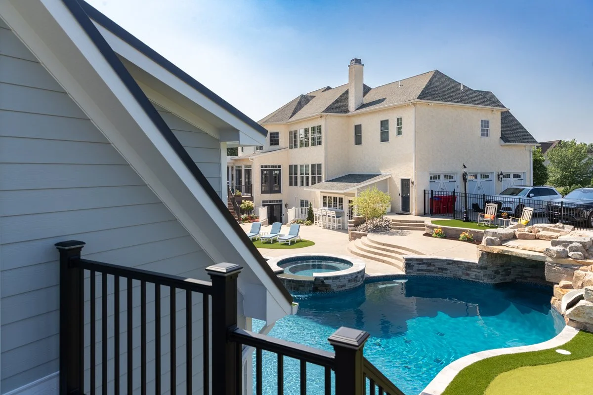 Large backyard with swimming pool, hot tub, and outdoor seating areas, surrounded by a white house with multiple floors and garages.