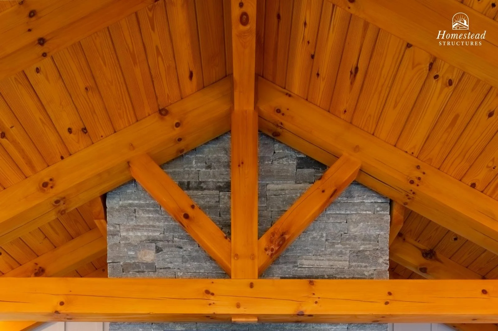Interior view of a wooden ceiling with exposed beams and a stone chimney.