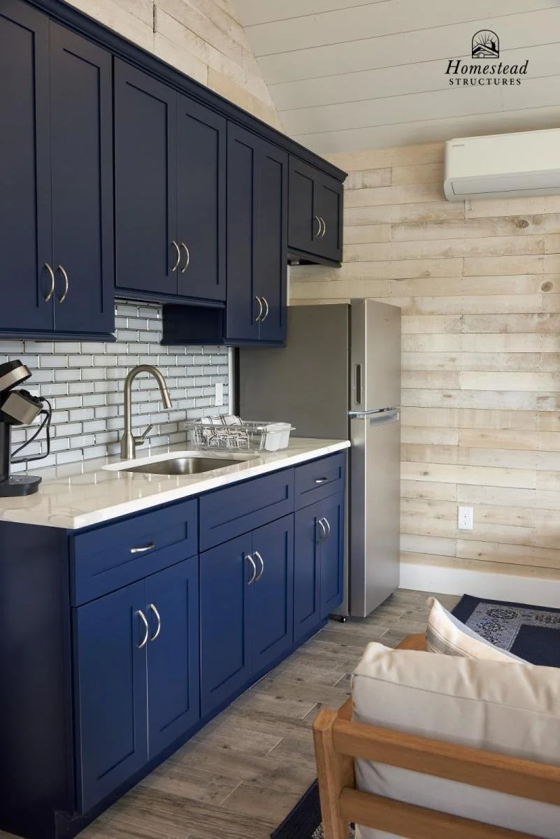 Kitchen with blue cabinets, white countertop, gray refrigerator, white tiled backsplash, and wooden wall, with an air conditioner on the wall.