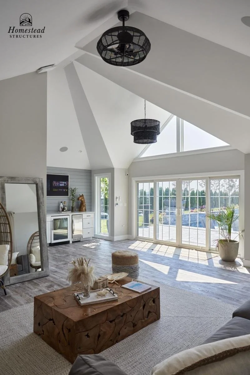 Bright living room with vaulted ceiling, large sliding glass doors, and modern decor including a wooden coffee table, a large mirror, and potted plants.