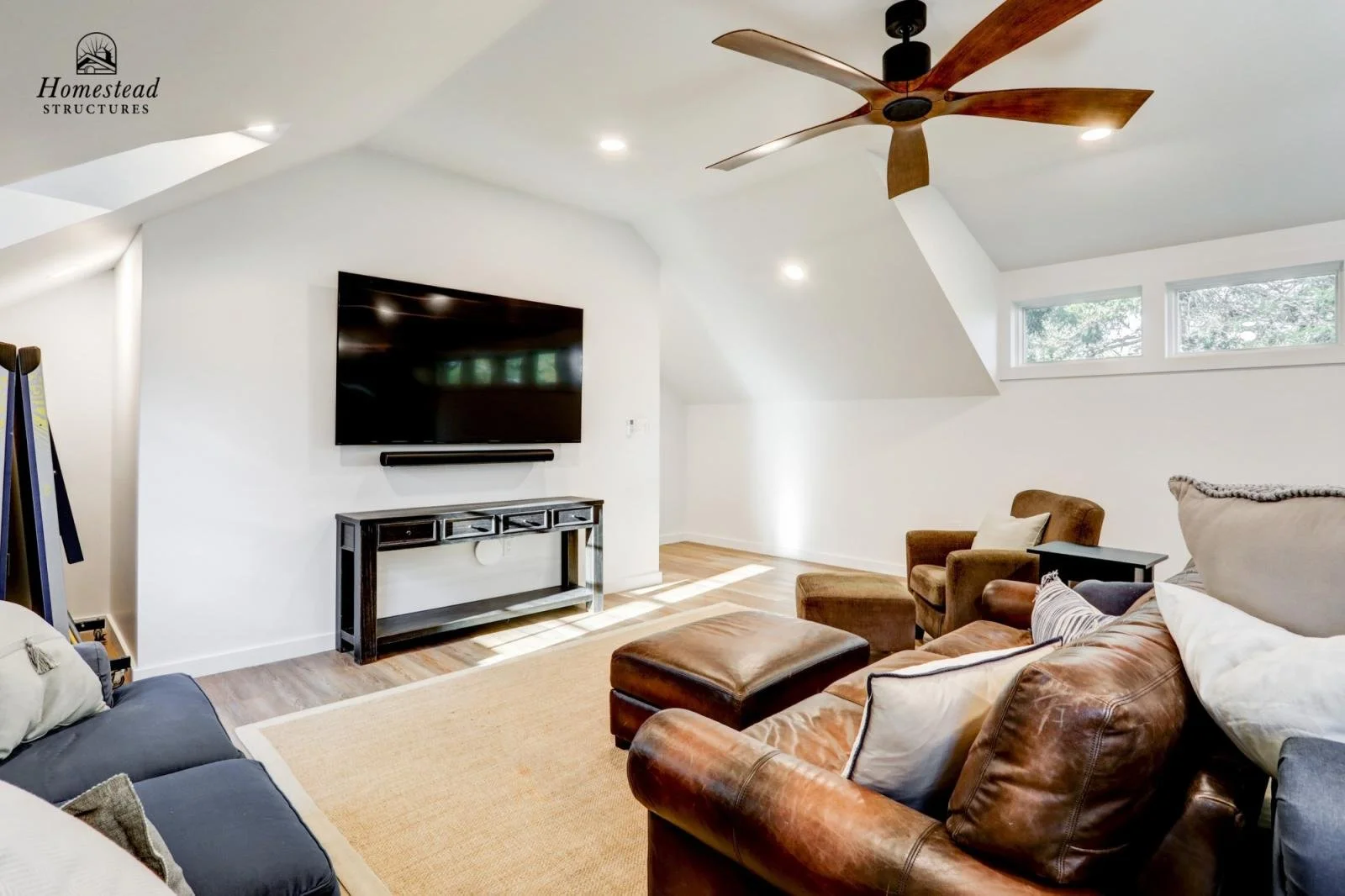 Living room with white walls, wooden flooring, a television mounted on the wall, and brown leather and upholstered chairs and sofas.
