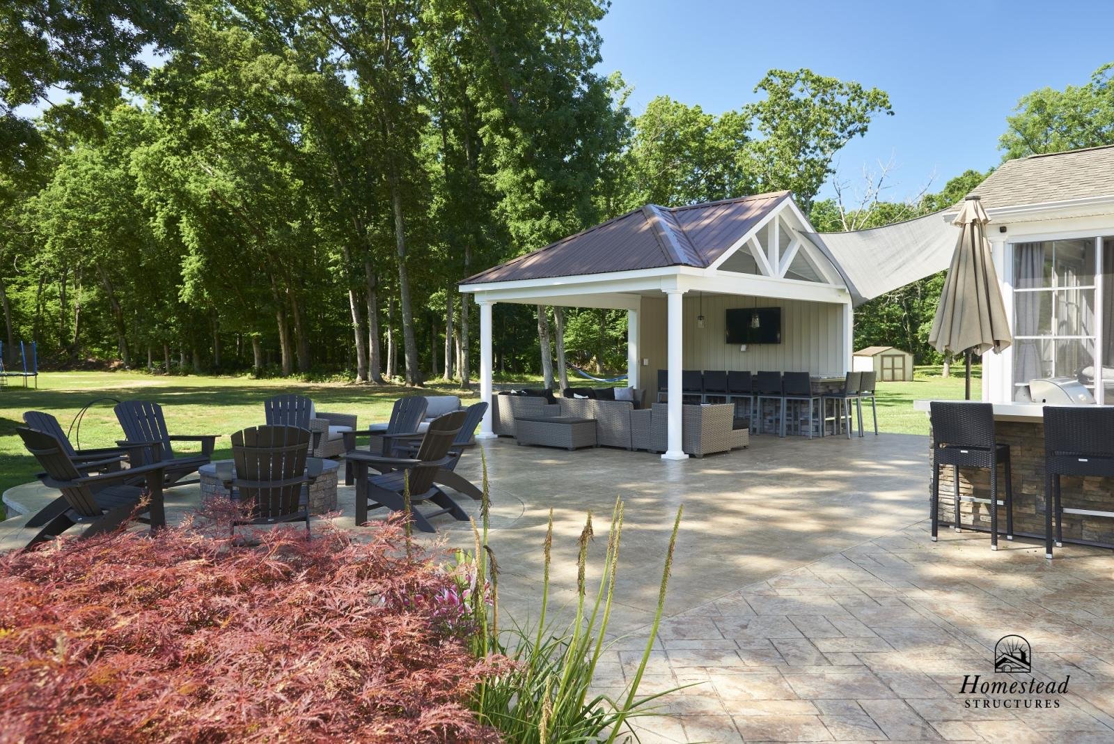 Outdoor patio area with seating, a fire pit, a bar, and a screened porch, surrounded by trees