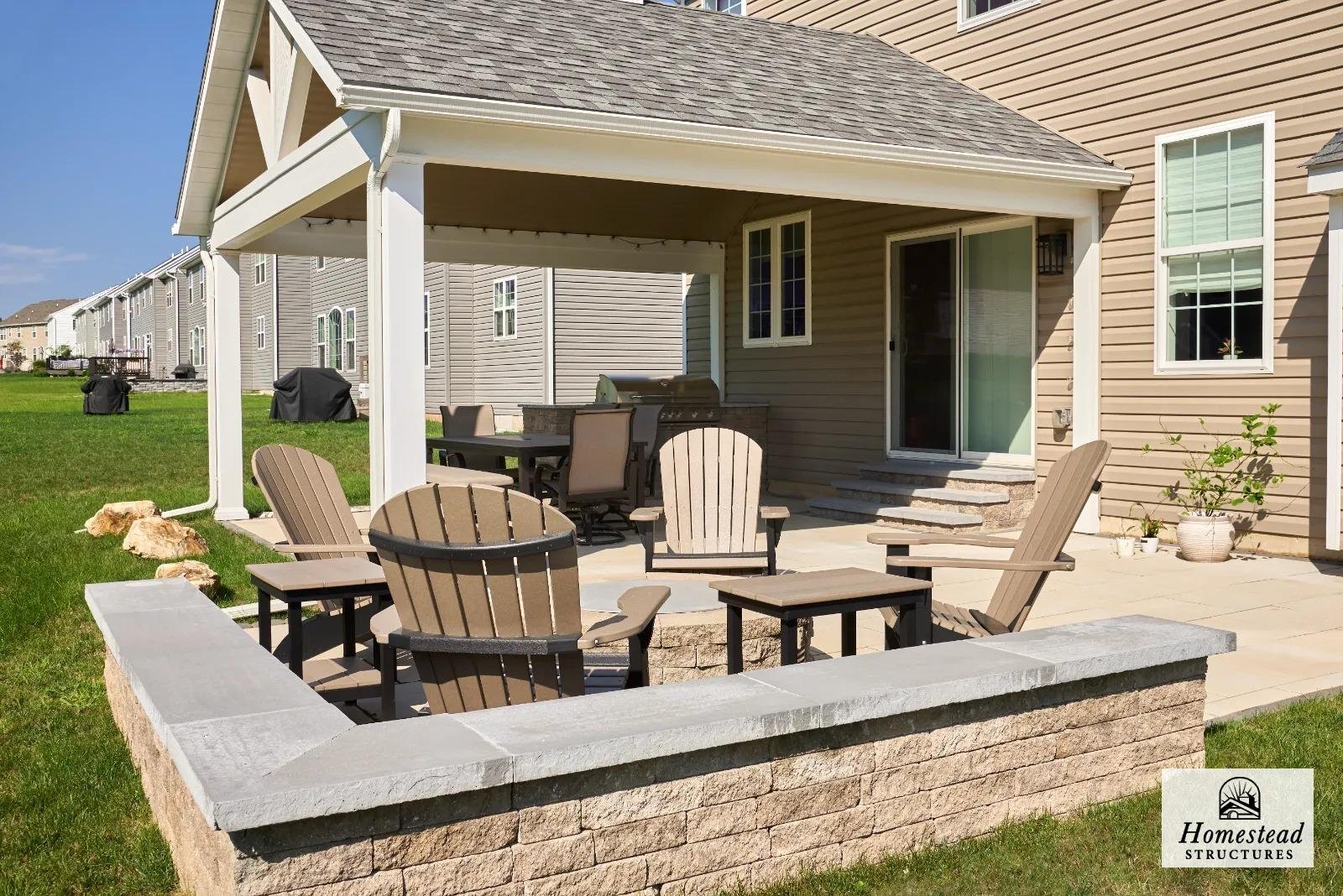 Backyard patio with outdoor furniture and a covered area of a suburban house, with a grassy lawn and neighboring houses visible in the background.