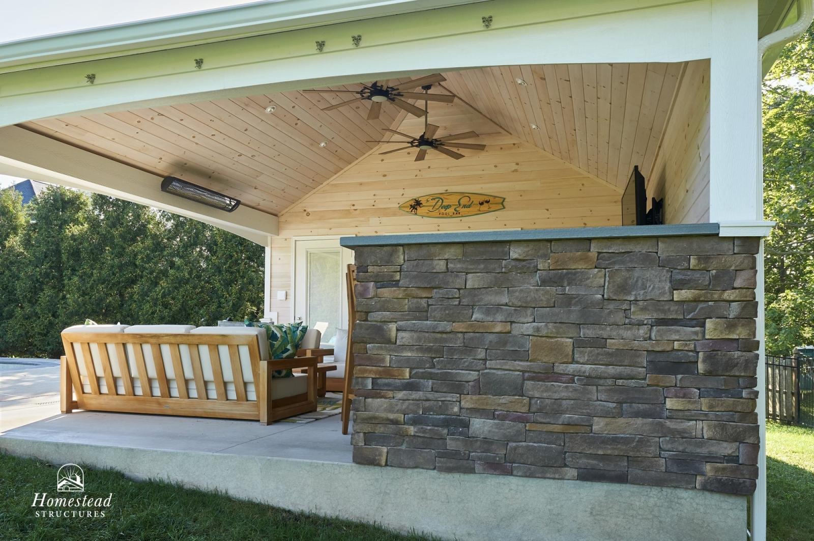 Covered outdoor patio with wooden ceiling fans, a stone half wall, outdoor furniture, and a surfboard sign that reads "Dare End."