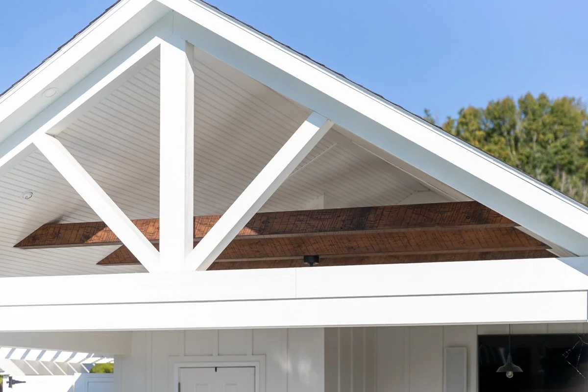 Close-up of a modern house's front gable with white siding, exposed wooden beams, and a clear blue sky overhead.