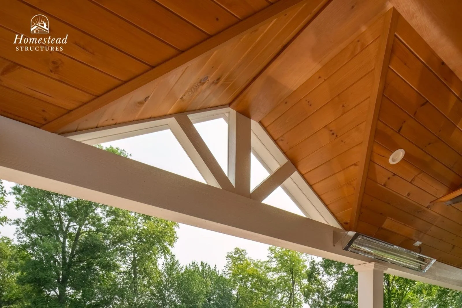 Close-up of a wooden ceiling with exposed beams and triangular window framing, with greenery visible outside.