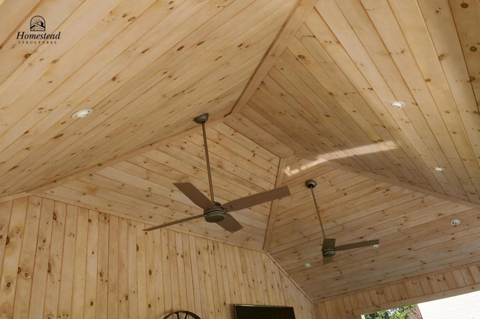 Wood-paneled ceiling with two ceiling fans and recessed lighting in a home interior.