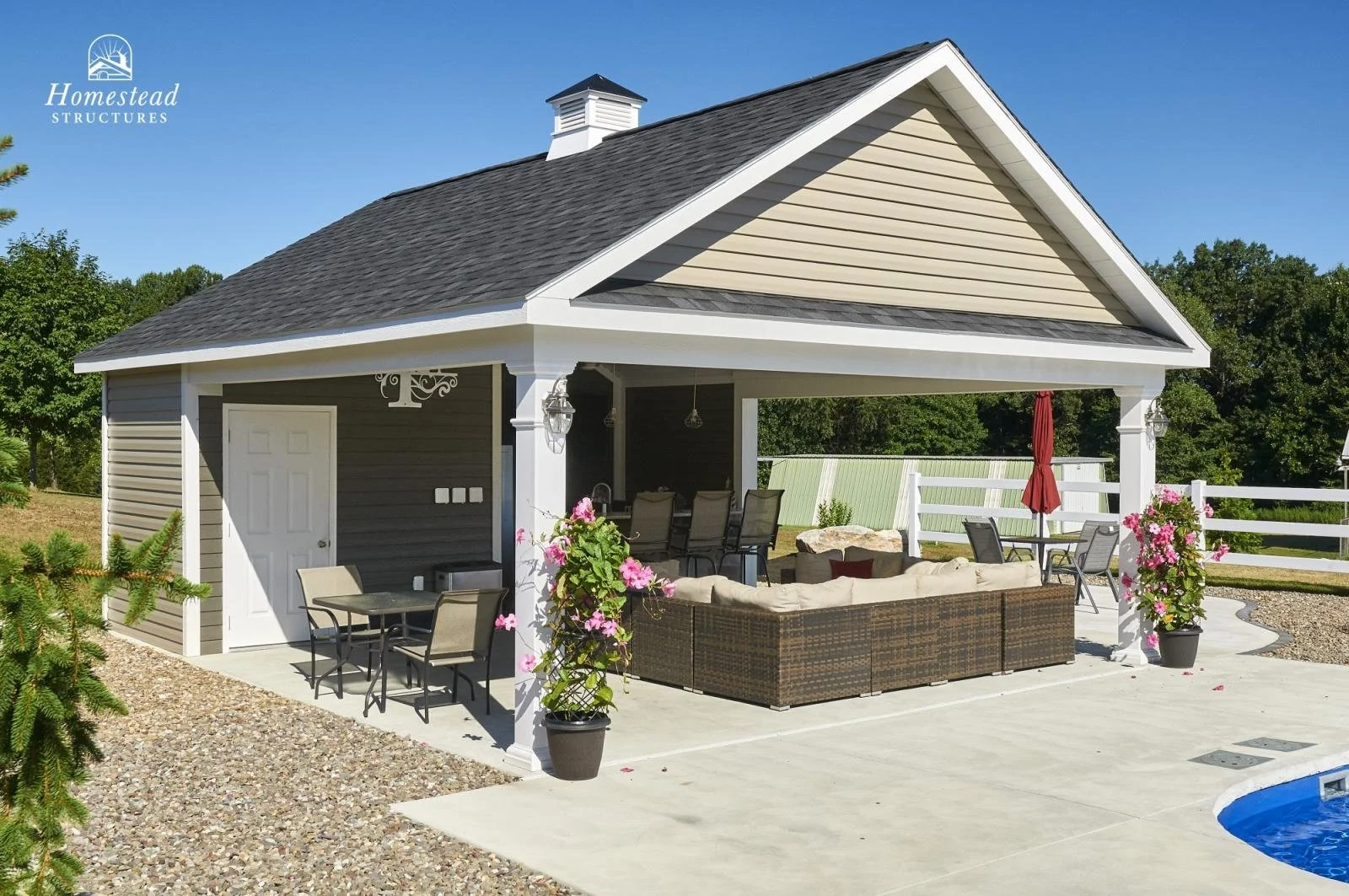 A backyard patio with outdoor furniture, potted flowers, and a nearby swimming pool under a clear blue sky.