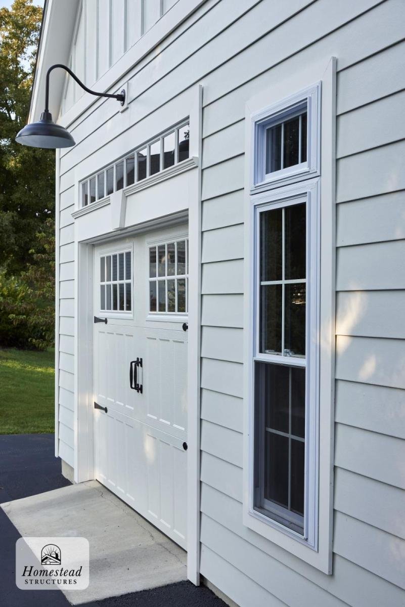 Exterior of a white garage with double doors and two vertical windows on the right, siding, and an outdoor light fixture above the door.