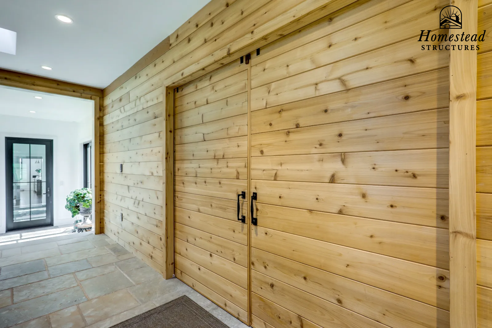 Interior view of a home with wood paneled walls, tile flooring, and a glass door leading outside, with a potted plant visible near the entrance.