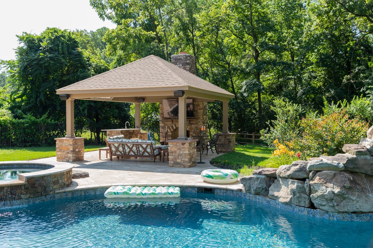 Backyard with swimming pool, pool floats, and a shaded outdoor seating area with a stone chimney and television