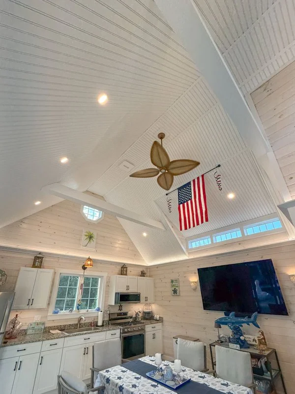 A kitchen and dining area with a vaulted ceiling, ceiling fan, American flag, and a flat-screen TV on the wall.