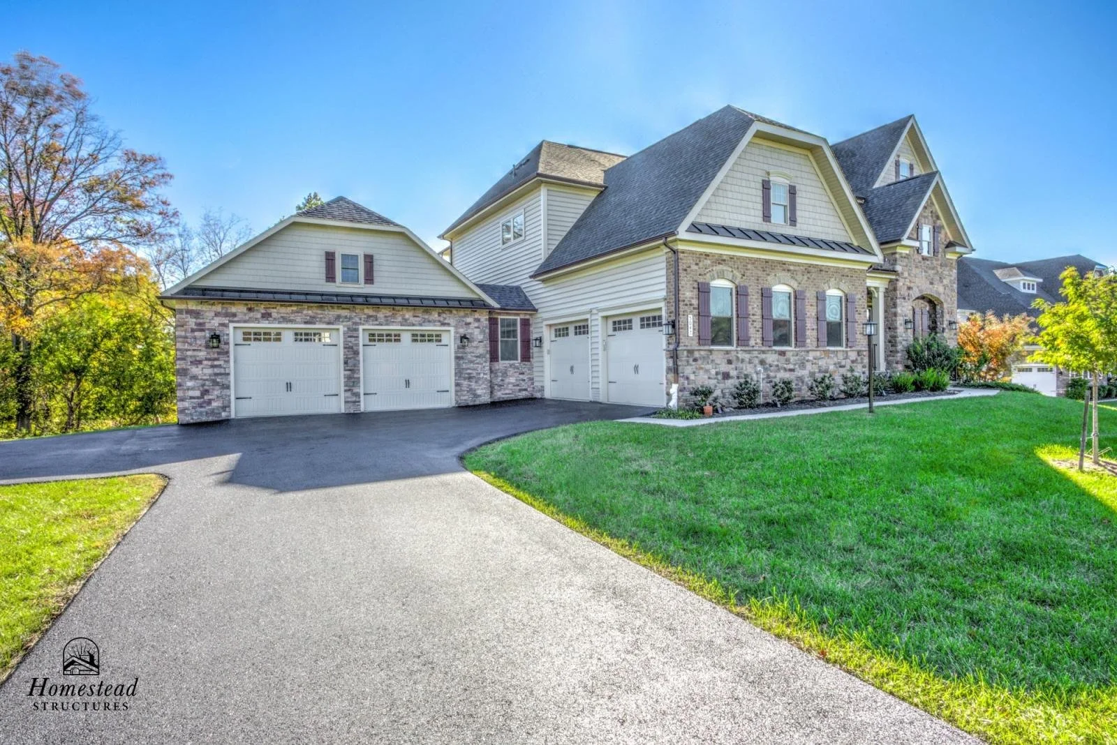 Front view of a large, modern house with a well-maintained lawn, brick and siding exterior, three-car garage, and clear blue sky.