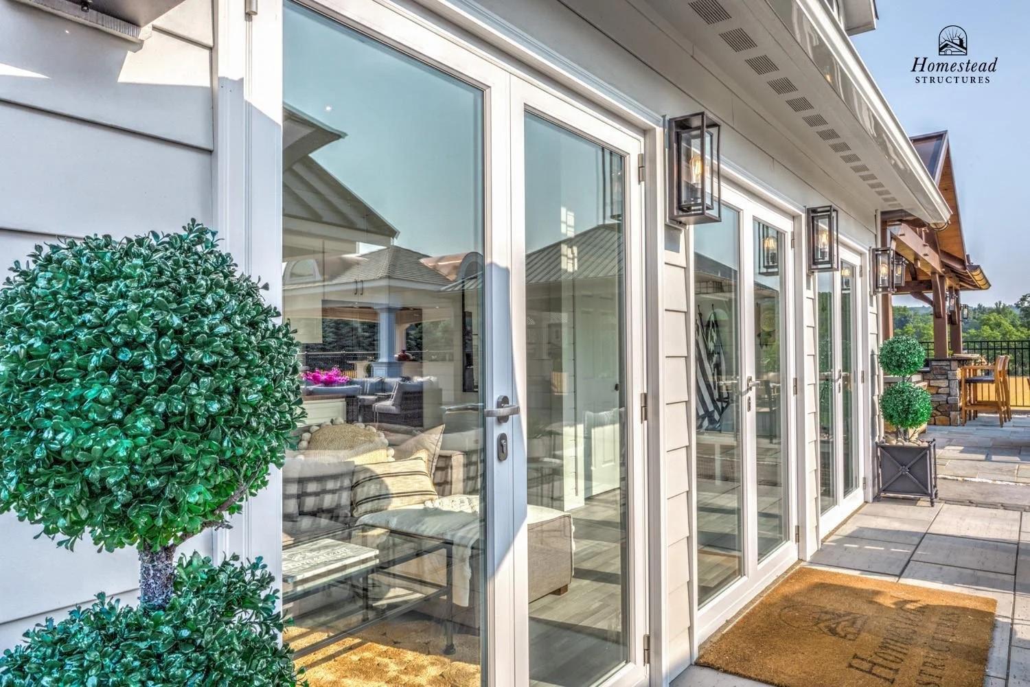 Exterior view of a house with large glass sliding doors, outdoor lanterns, and potted topiary plants on a patio.