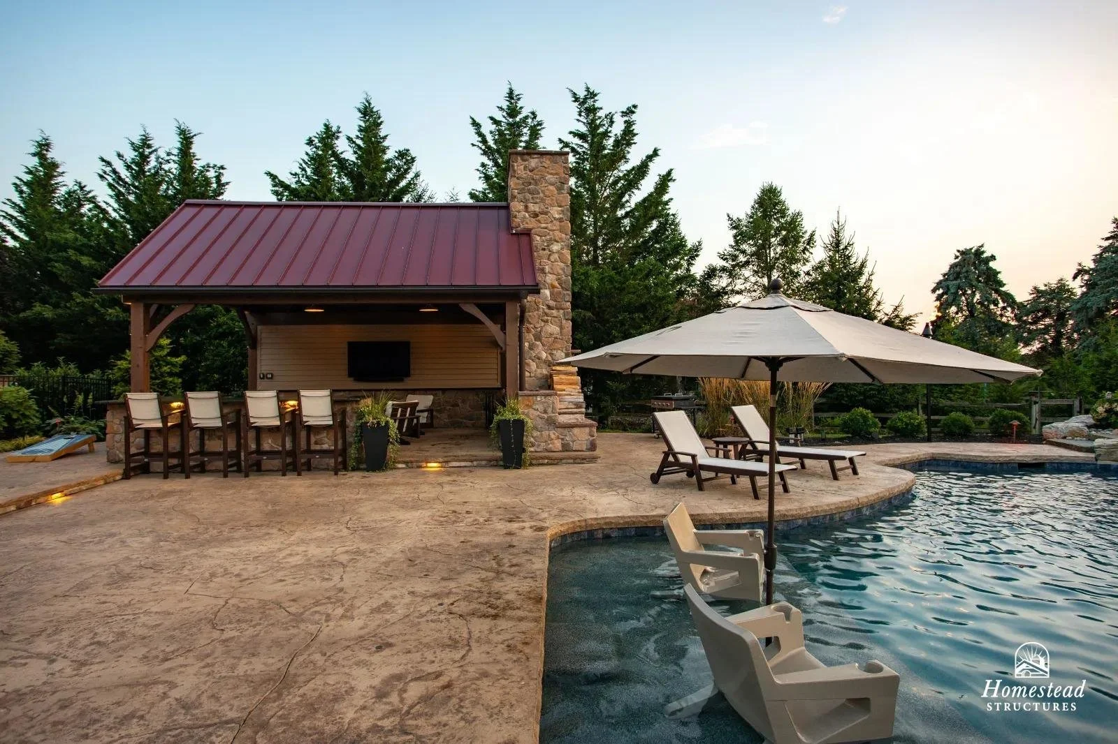 A backyard with a pool, an umbrella, and outdoor furniture including lounge chairs and a building with a red metal roof and a stone chimney.