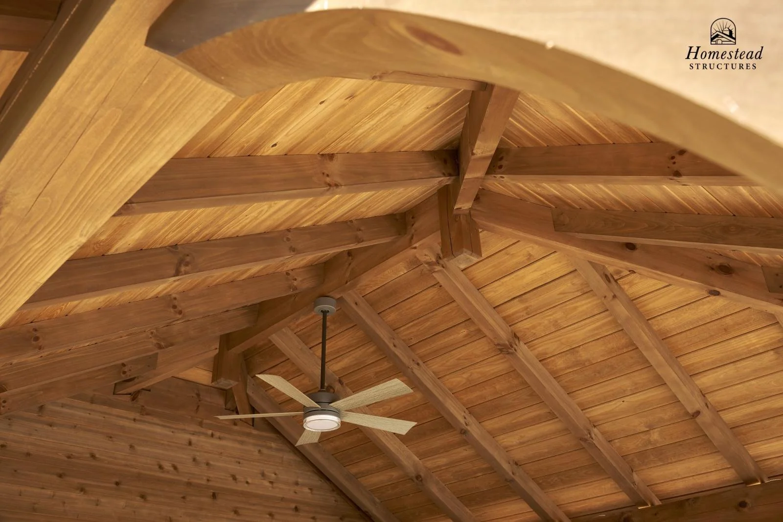 Wooden ceiling with exposed beams and a ceiling fan. The image features a natural wood finish with visible grain and knots. The ceiling fan has five blades and is mounted in the center of the ceiling.