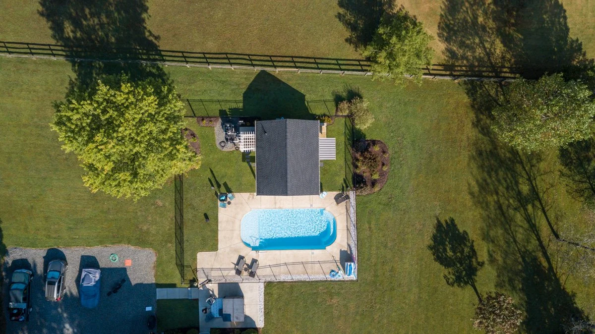 Aerial view of a backyard with a swimming pool, patio furniture, and surrounding greenery.