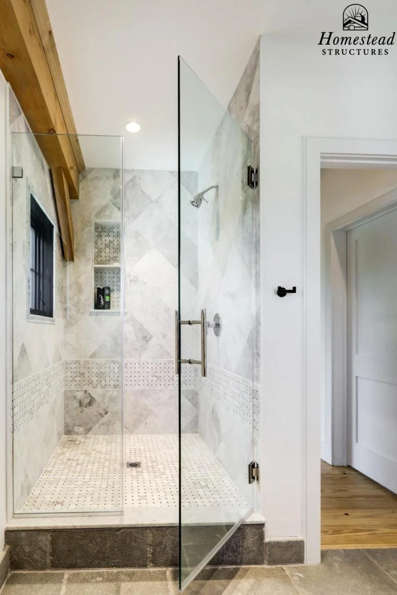 Modern walk-in shower with glass door, tiled walls and floor, showerhead, small window, built-in shelves, and wooden ceiling beams.