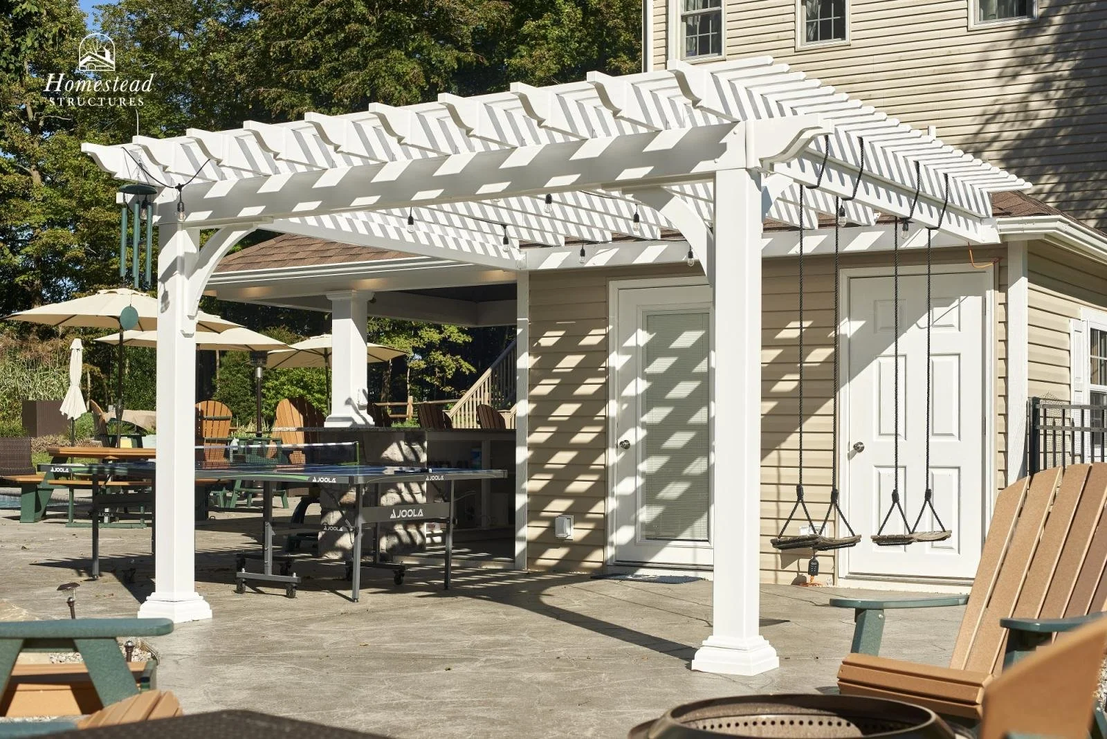 An outdoor patio area with a white pergola, swings hanging from the pergola, and various outdoor furniture including umbrella-shaded tables and chairs.