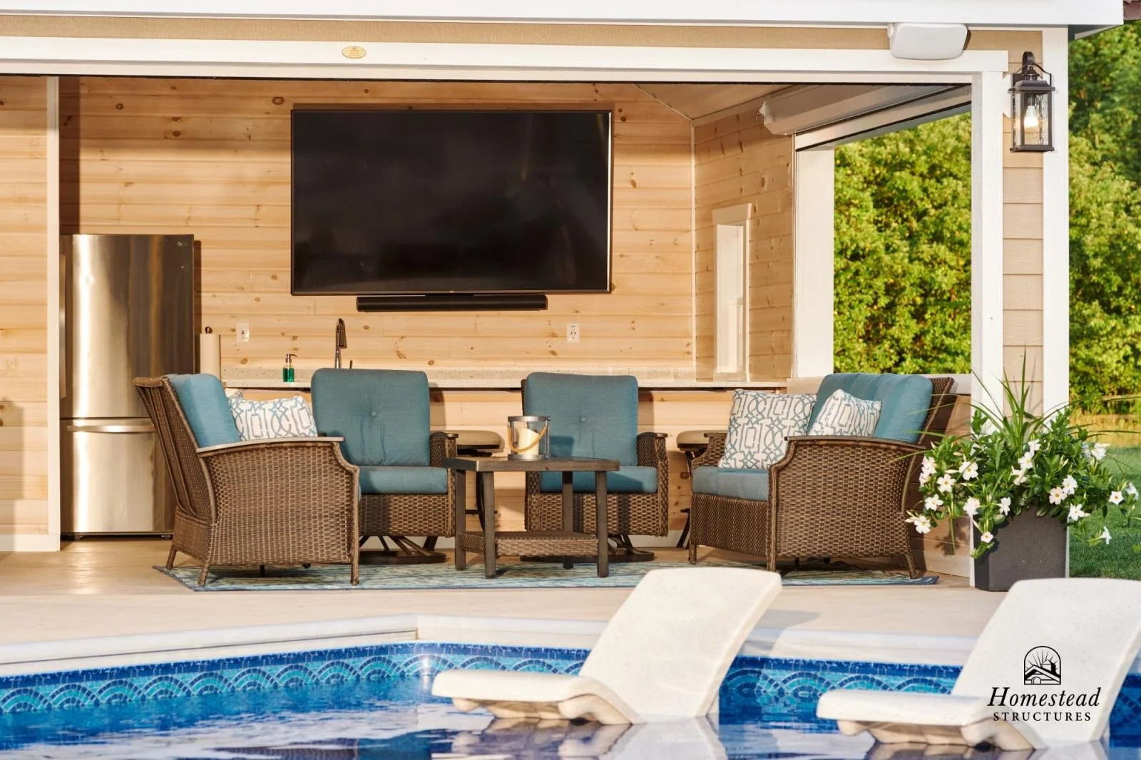 Outdoor poolside patio area with wicker seating, a flat-screen TV, and a large window overlooking greenery.