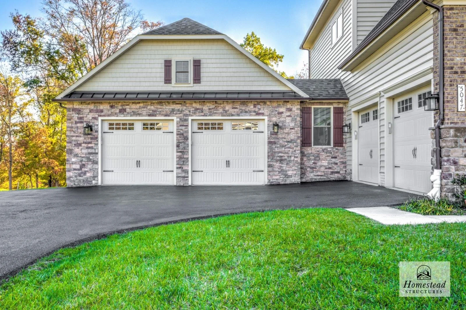 Front of a house with three white garage doors, brick and siding exterior, a window with shutters, and a lawn with green grass.