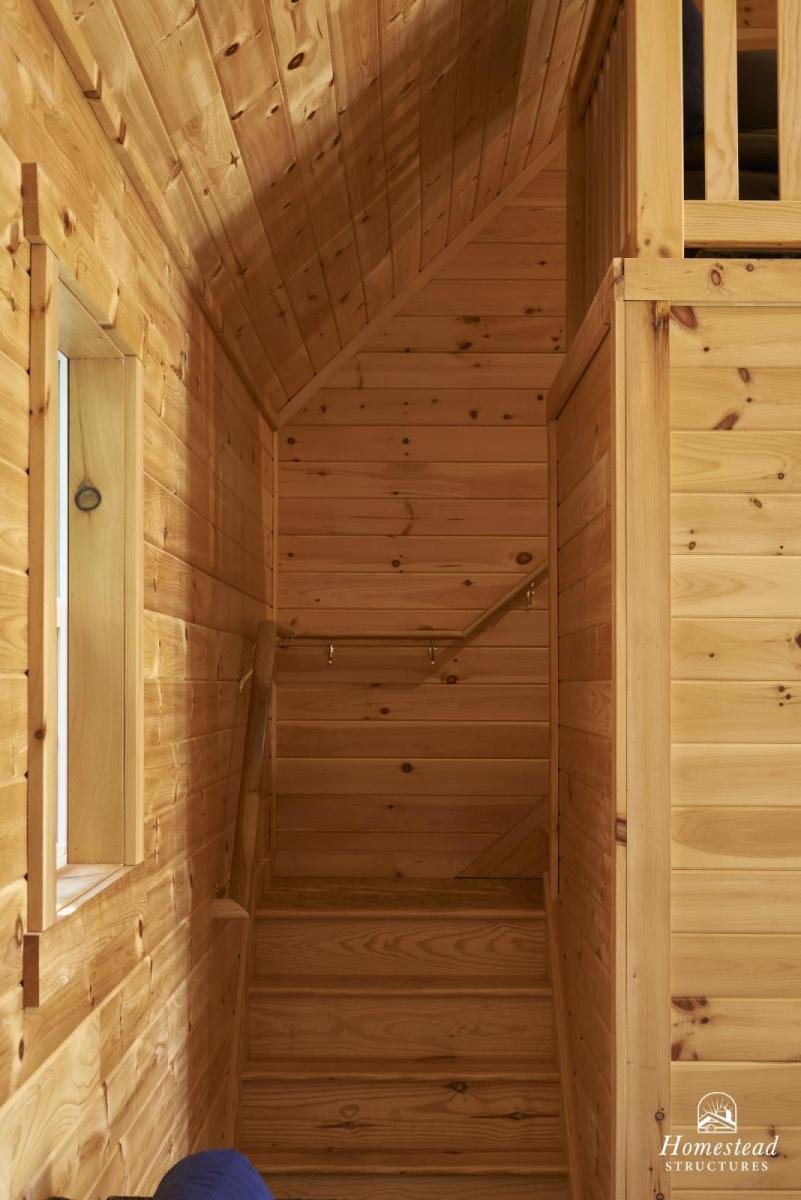 Interior view of a wooden staircase made from natural wood planks with a small window on the left wall.