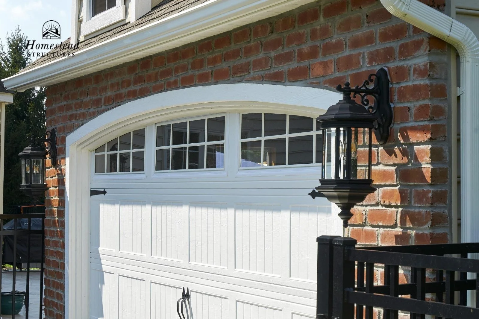 Close-up of a brick house exterior with white garage door, black outdoor wall lanterns, and a white gutter system.