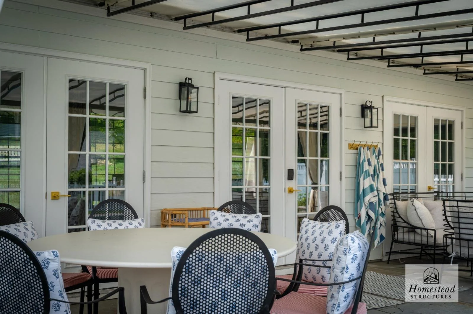 Covered porch with black and white furniture, wicker chairs, a large round table, and outdoor curtains.