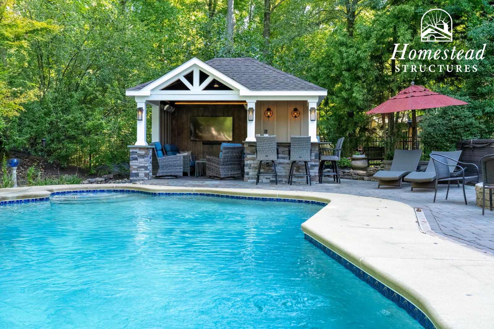 A backyard with a swimming pool, outdoor seating, and a small pavilion with a TV, surrounded by trees, with a logo for Homestead Structures in the top right corner.