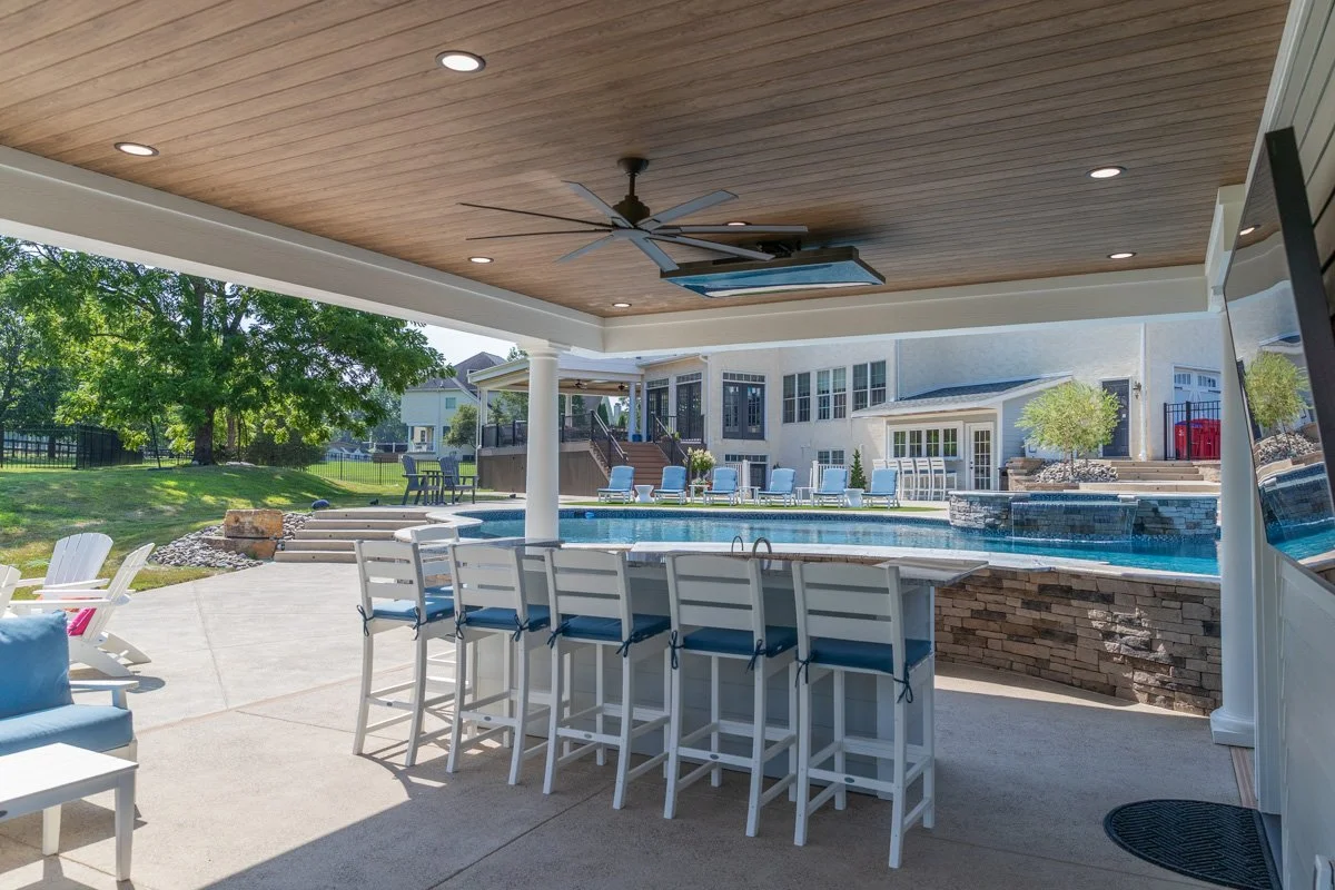 View of a backyard with a swimming pool, outdoor seating, and a covered patio area with a wooden ceiling and ceiling fan.