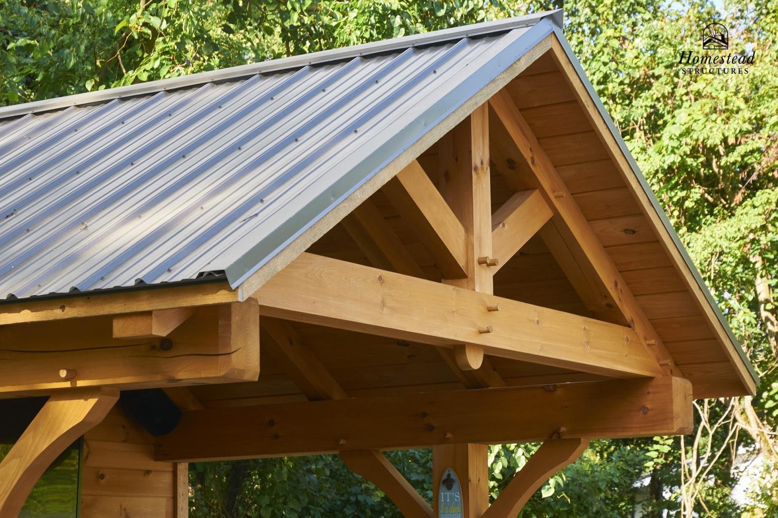 Close-up view of a wooden structure with a metal roof, surrounded by green trees.