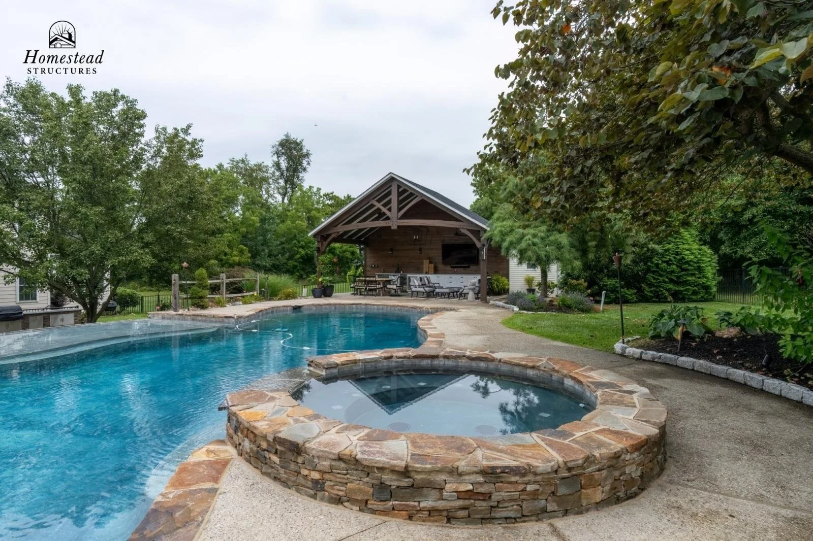 Backyard with a large swimming pool, hot tub, and a covered patio area with outdoor furniture, surrounded by trees and landscaping.