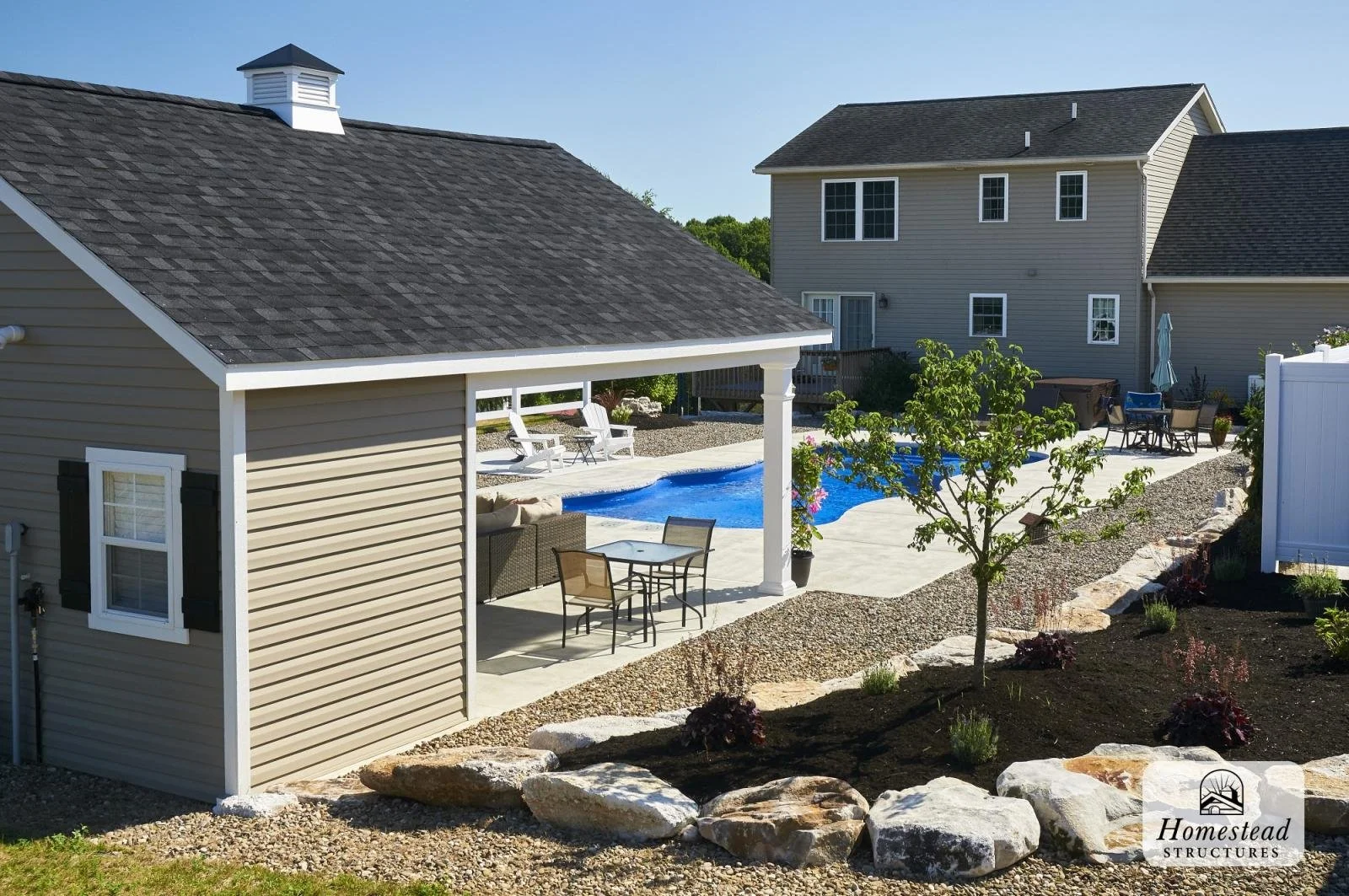 Backyard with in-ground pool, patio furniture, small trees, and a shed surrounded by gravel and landscaping.