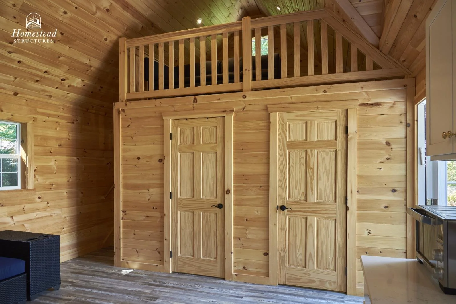 Interior of a wooden cabin with two doors underneath a loft, wooden walls, and floor, with a small window on the left and a microwave on the right.